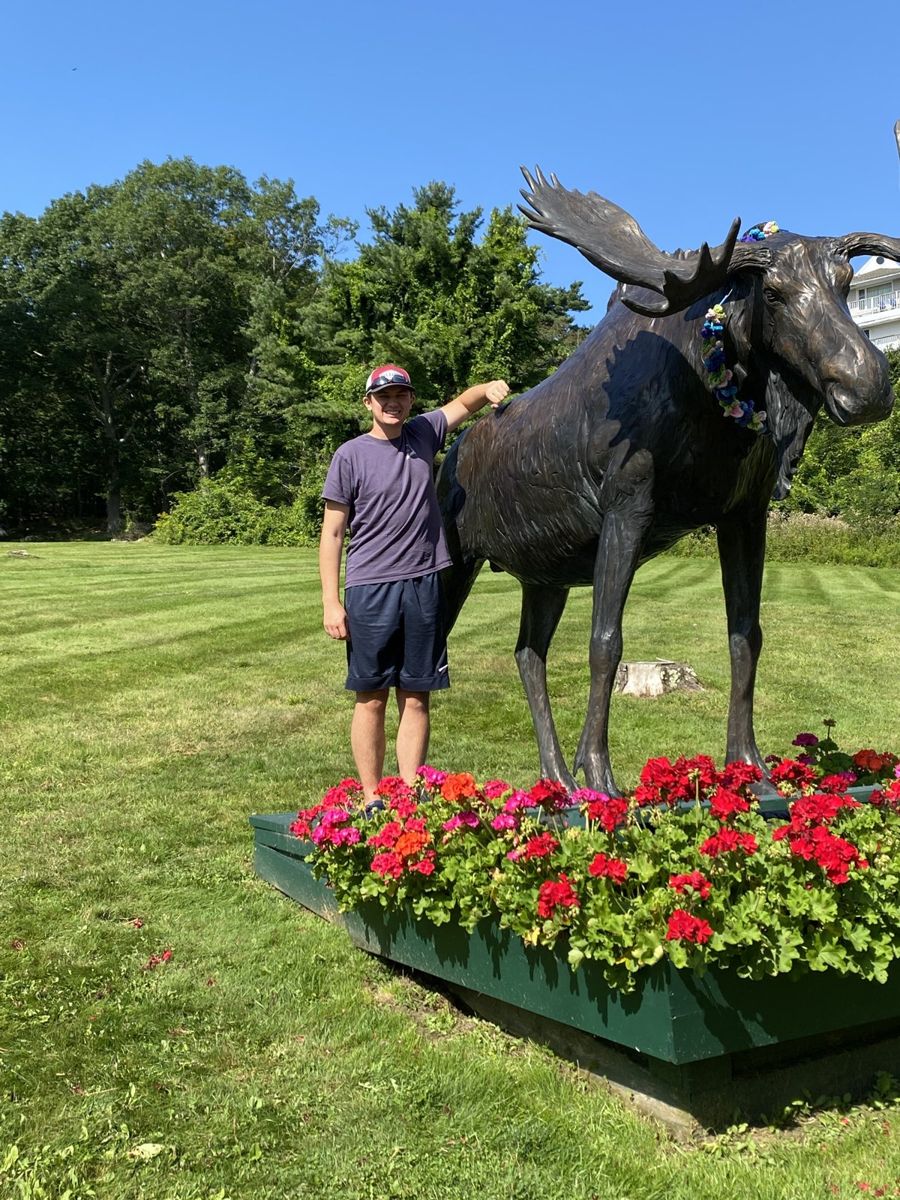 Alex standing beside a bronze moose statue on a sunny lawn